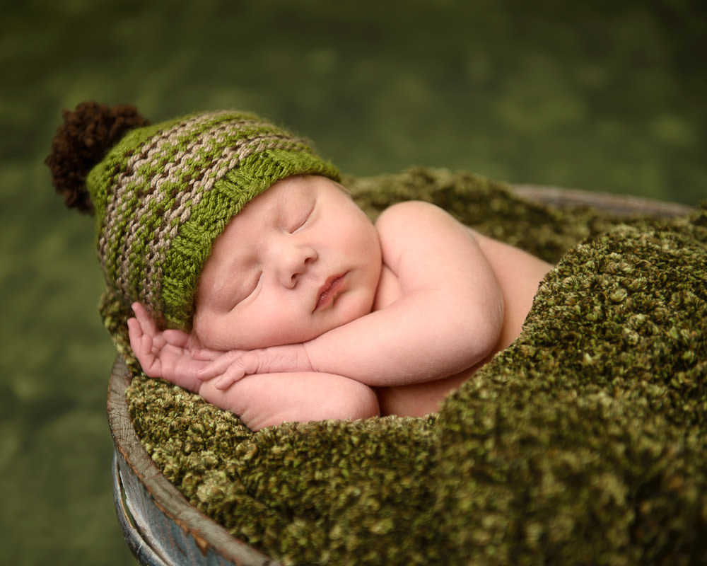Newborn Baby Boy photography in a bucket wrapped in deep green colors
